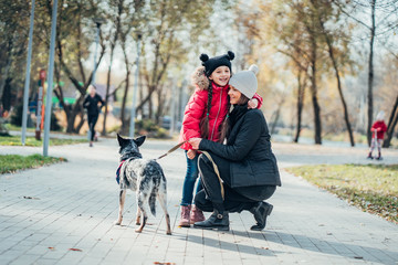 Happy mother and her daughter walk with dog in autumn park