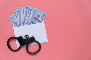 handcuffs with money in an envelope on a pink background