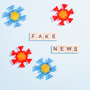 Words Fake News Made Of Wooden Blocks With Coronavirus Model On Blue Background, Flat Lay, Top View. Fake News About Pandemic Concept, Disinformation In Social Media Theme