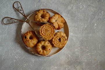 Small, curly cupcakes with raisins and chocolate drops inside, lie on a ceramic plate with pastry tongs. Top view, copy space, close-up..