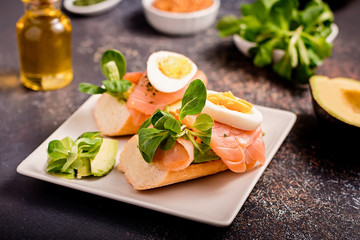 Healthy toasts with smoked salmon and avocado served with mustard, eggs and leafy greens on black table top. Mediterranean diet snack, open sandwich