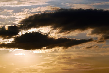 Bright orange sun behind clouds during a beautiful evening sunset. Beautiful landscape in the evening