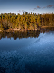 Fototapeta na wymiar Ice forming in the cold waters of a remote lake surrounded by denseforest