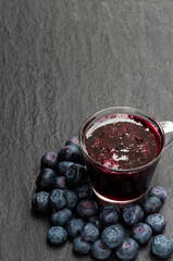 Homemade blueberry jam in glass cup on black stone background