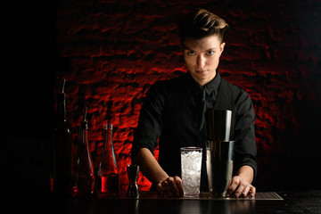 bartender stands in dark bar with different bar equipment on bar counter.