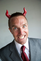 Mischievous businessman with red devil horns looking at the camera with a devilish grimace