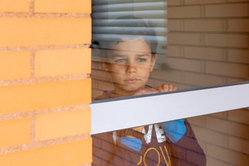 Close up of sad boy inside home looking out the window.