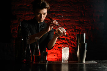 young woman bartender in black clothes actively breaks ice with special device.