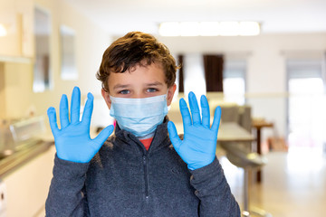 Boy wearing surgical mask and blue gloves holding hands up showing palms.