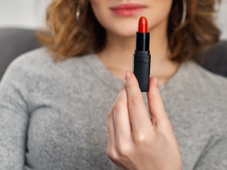 Woman's beauty blogger hands holding professional hi-end red lipstick with blurred body background,...