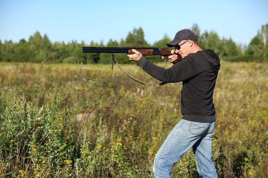 man standing with rifle. hunter in a baseball cap and black sunglasses takes aim from a gun. summer hunt