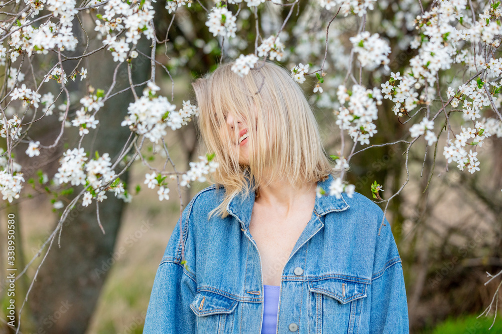 Sticker Blonde woman in denim clothes next to blooming tree