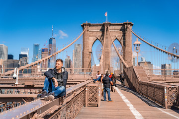 Young man sitting on a  Brooklyn Bridge with a magical Manhattan island view.