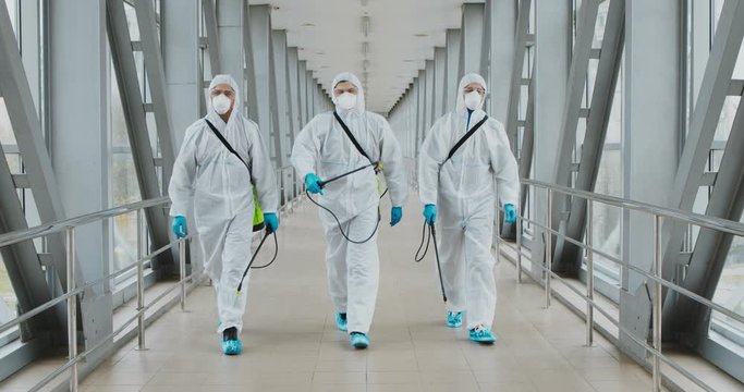 Group of disinfectors in hazmats walking in public building