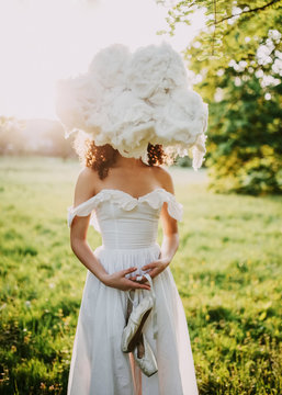 Young Woman Wearing A White Maxi Dress, Holding Artificial Clouds. Concept Of Cloudy Weather And Meteorology. Head In The Clouds.