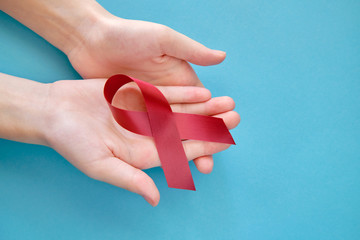 Dark red symbolic ribbon - the problem of disabled people and amyloidosis. Two crossed hands on a blue background