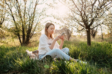 Young woman with a smartphone, sitting on grass in a garden, backyard.