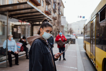 Young woman wearing surgical mask outdoor at bus stop in the street
