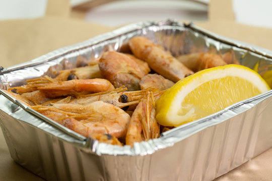 Close-up of shrimp in a foil box for delivery and a paper bag on a white background.