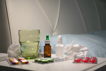 Tablets, medicines, nose drops, tissues on the bedside table beside the bed. Concept of home outpatient treatment of coronavirus.