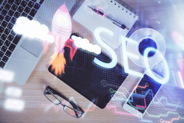 Double exposure of SEO hologram drawing over desktop. Top view. Search optimization concept.