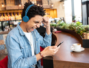 Man smiling while looking at the phone in a cafe with a cup of coffee.