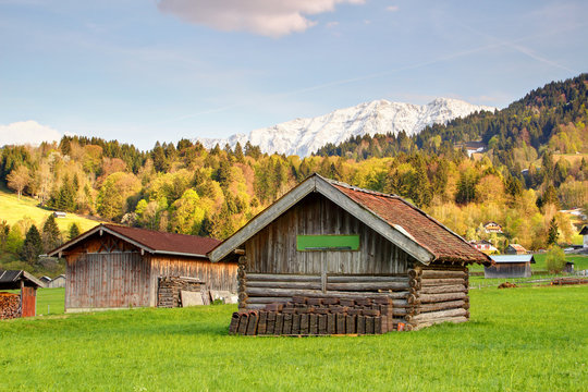 Bavarian rural scenery of typical timber hay barns with sunny forests and snowy peaks of Wetterstein mountain range in background, Hausberg Garmisch Partenkirchen Bayern Germany Europe