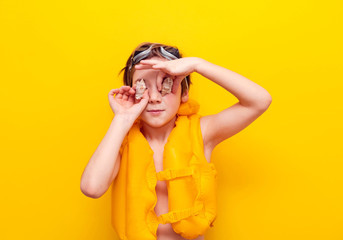 Rest and travel to the sea with a child. Cheerful boy in an inflatable vest on a yellow background with shells. Swimming in the pool, relaxation in the water park.