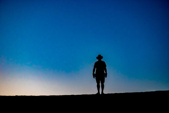 Silhouette in the desert at sunset of a man with water bottles resembles cowboy of the old west.