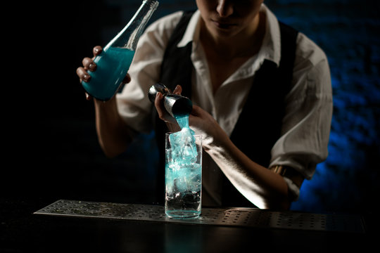 professional bartender masterly pours blue drink into glass on bar counter.