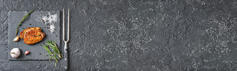 Slate plate with cooked pork steak and spices on dark background with space for text