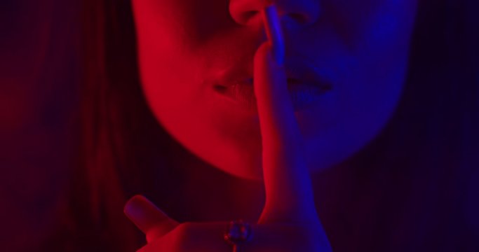 A beautiful girl is standing in blue and red neon light and sexually puts her finger to her lips . Close-up shooting. 4K