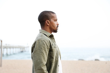 Back young man walking on beach towards water wearing casual clothing. Outdoor.