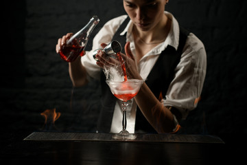 professional bartender masterly pours drink into smoky glass on bar counter.