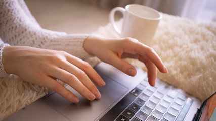 Image of girls hands typing on the couch at home.  Work from home. Working on laptop computer with cup of coffee. Selective focus