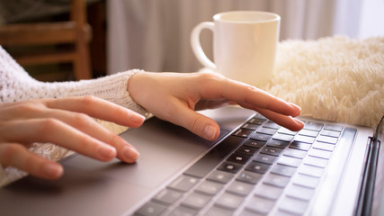 Image of girls hands typing on the couch at home.  Work from home. Working on laptop computer with cup of coffee. Selective focus