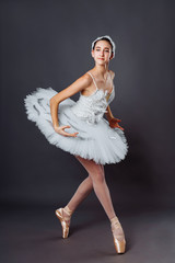 Fototapeta premium Classical Ballet dancer portrait. Beautiful graceful ballerina in white tutu from Swan lake practice releve ballet position in the studio. Vertical image of gifted young teenager in pointe on hippies
