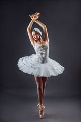 Ballerina dancing in white dress. Color photo. Graceful ballet dancer or classic ballerina dancing isolated on grey studio background. Ballerina on point shoes feet tutu from Lake Swan - obrazy, fototapety, plakaty