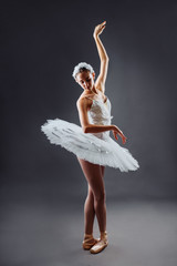A young graceful ballerina dressed in professional attire, pointe shoes and a white tutu, demonstrates dance skills. Beautiful classic ballet dancer isolated on grey backgroung in photostudio