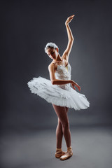 A young graceful ballerina dressed in professional attire, pointe shoes and a white tutu,...