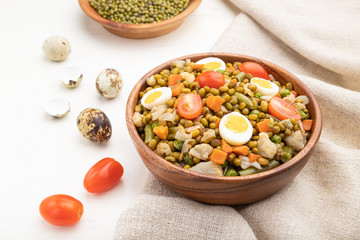 Mung bean porridge with quail eggs, tomatoes and microgreen sprouts on a white wooden background. Side view, close up.