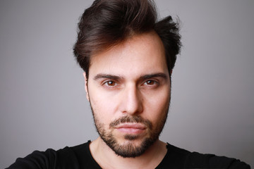 Headshot of serious stylish man looks straight with confident expression, posing on grey background.