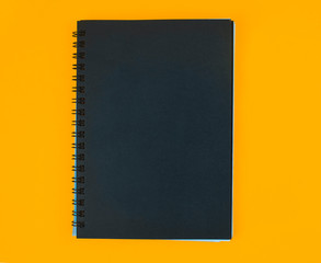 Fototapeta premium A diary of black color cover placed on an isolated orange paper background
