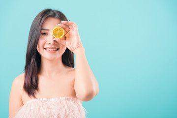 woman standing smile holding a piece of orange in front of her eye