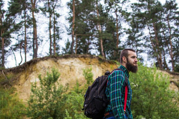 Naklejka na ściany i meble Handsome man hipster with beard on serious face in cloth shirt and suspenders sunny outdoor on mountain top against cloudy sky on natural. Tourism concept. Travel with a backpack. Wonderful landscape.