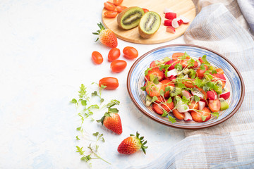 Vegetarian fruits and vegetables salad of strawberry, kiwi, tomatoes, microgreen sprouts on white concrete background. Side view, copy space.