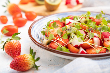 Vegetarian fruits and vegetables salad of strawberry, kiwi, tomatoes, microgreen sprouts on white concrete background. Side view, selective focus.