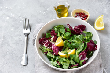 diet salad from radicchio, arugula, valerian leaves with lemon and olive oil in a white bowl on a gray background. vitamin diet salad recipe. selective focus, copy space