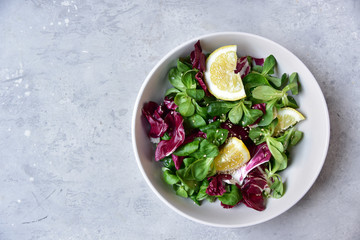 banner diet salad from radicchio, arugula, valerian leaves with lemon and olive oil in a white bowl on a gray background. vitamin diet salad recipe. selective focus, copy space