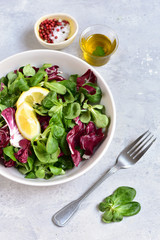 diet salad from radicchio, arugula, valerian leaves with lemon and olive oil in a white bowl on a gray background. vitamin diet salad recipe. selective focus, copy space